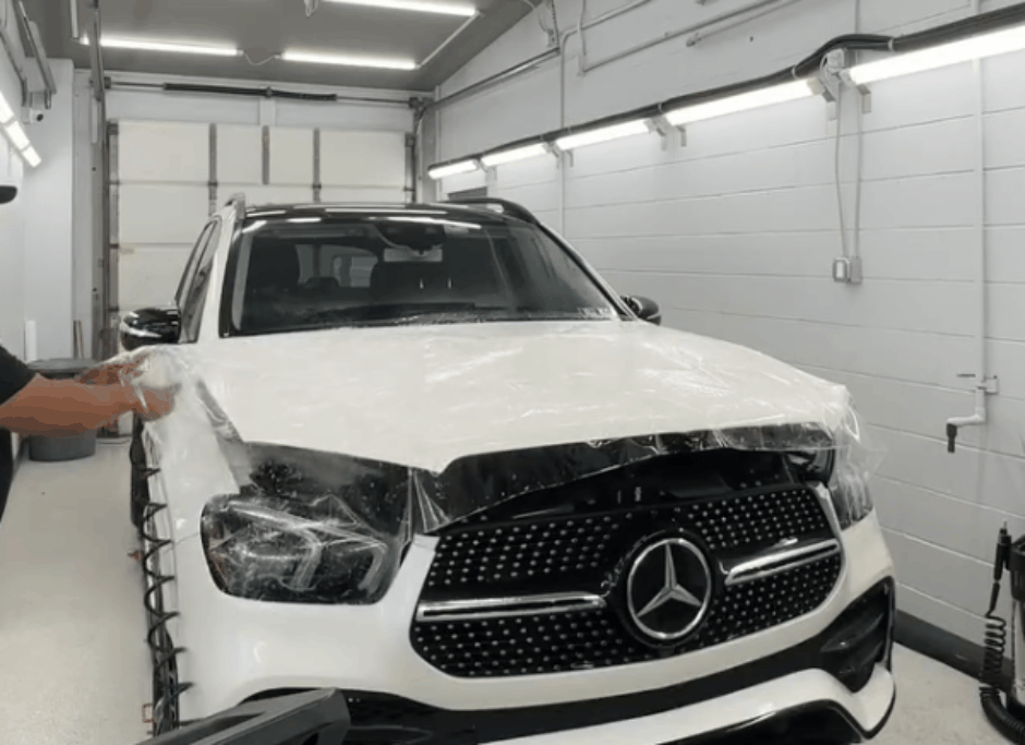 A technician carefully smoothing out a clear paint protection film (PPF) over the hood of a bright yellow car using a specialized tool, ensuring a flawless and bubble-free finish. The process underscores the benefits of professional PPF installation for long-lasting and seamless protection.