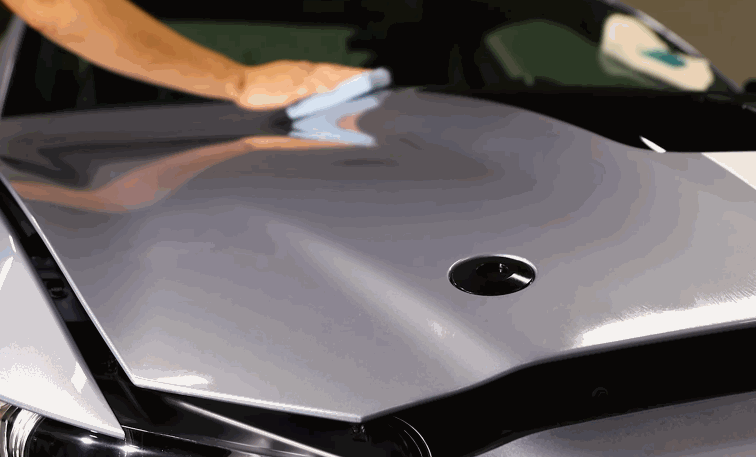 A technician uses a soft cloth to buff the surface of a silver car hood, bringing out a mirror-like shine