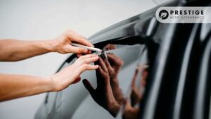 A professional applies window tint to a car’s side window, using a precision cutting tool to trim the film.